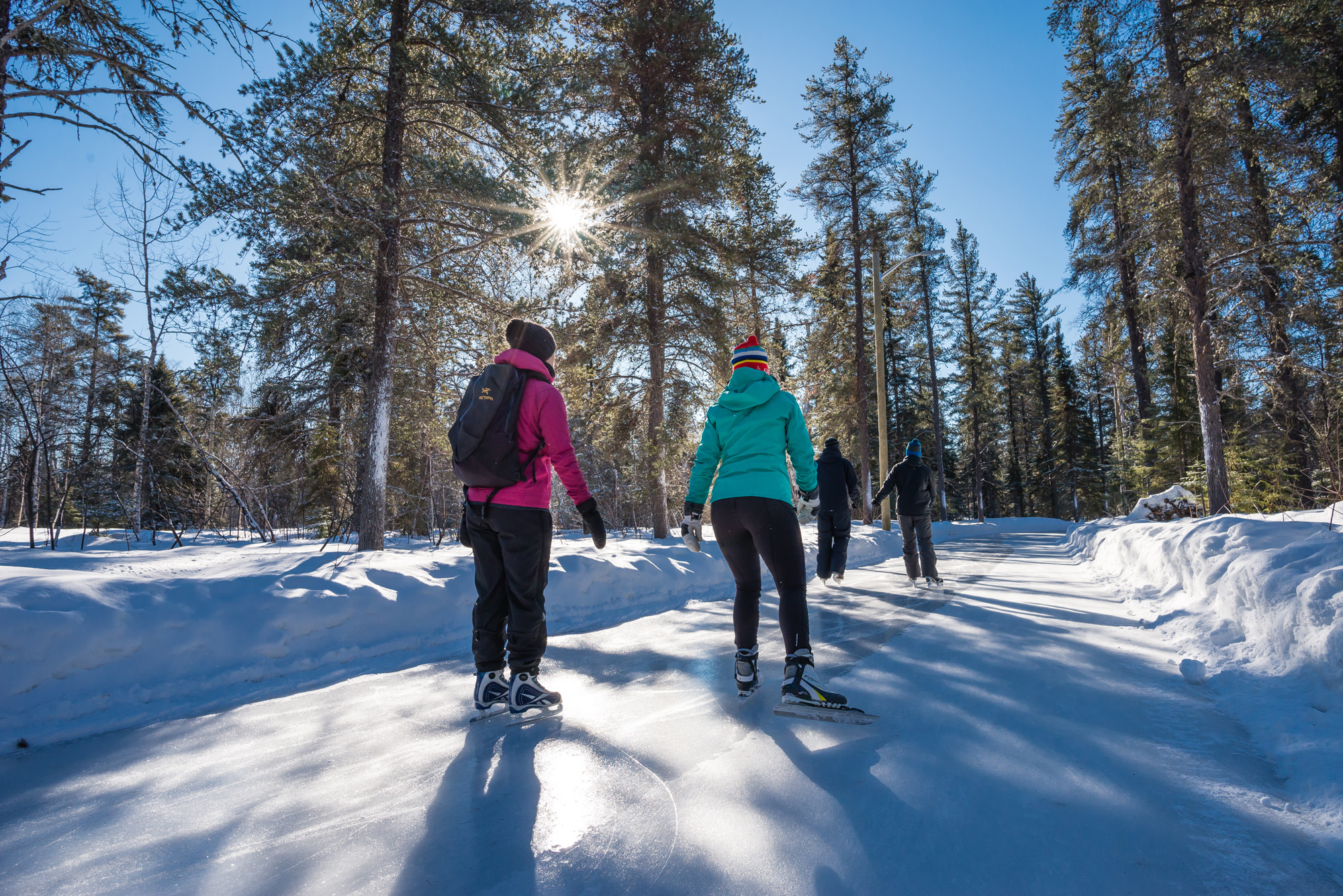 Le Sentier glacé Agnico-Eagle se trouve au coeur des activités hivernales de la Forêt récréative, à Val-d'Or, en Abitibi-Témiscamingue. Un groupe d'amis y patinent sous un ciel bleu et ensoleillé.